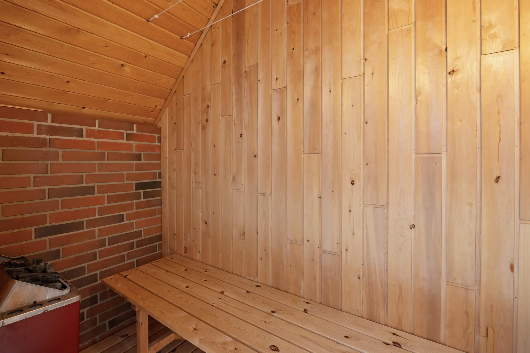 A wood-paneled sauna room with a long wooden bench beside a brick wall.