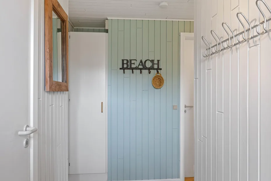A narrow hallway with pale blue paneling and wall hooks.