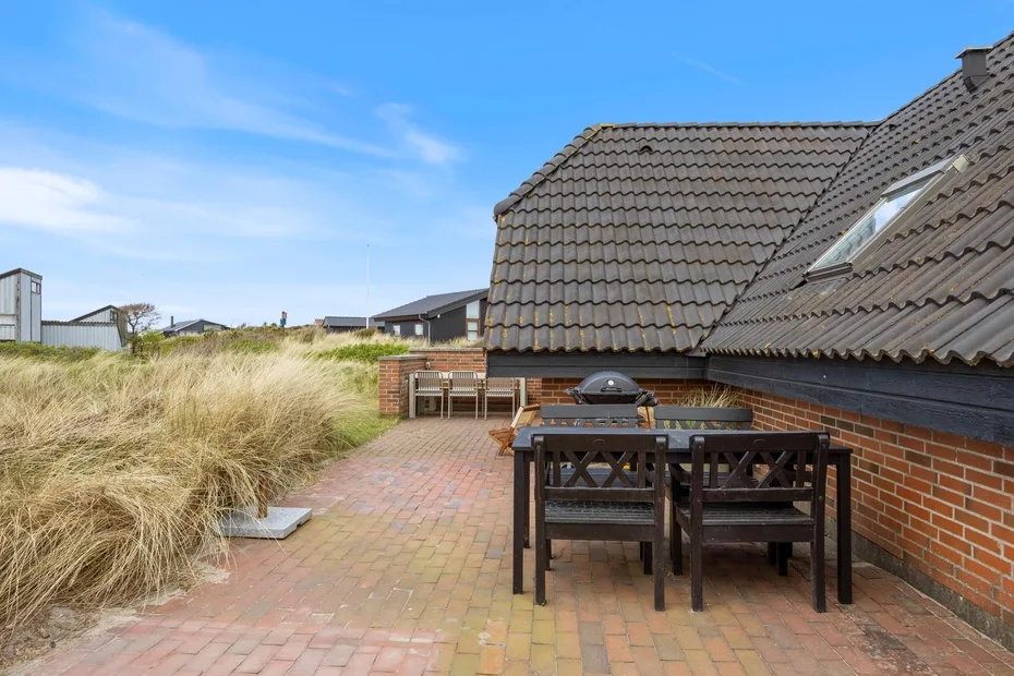 A brick-paved outdoor patio has a wooden dining set beside a brick building.