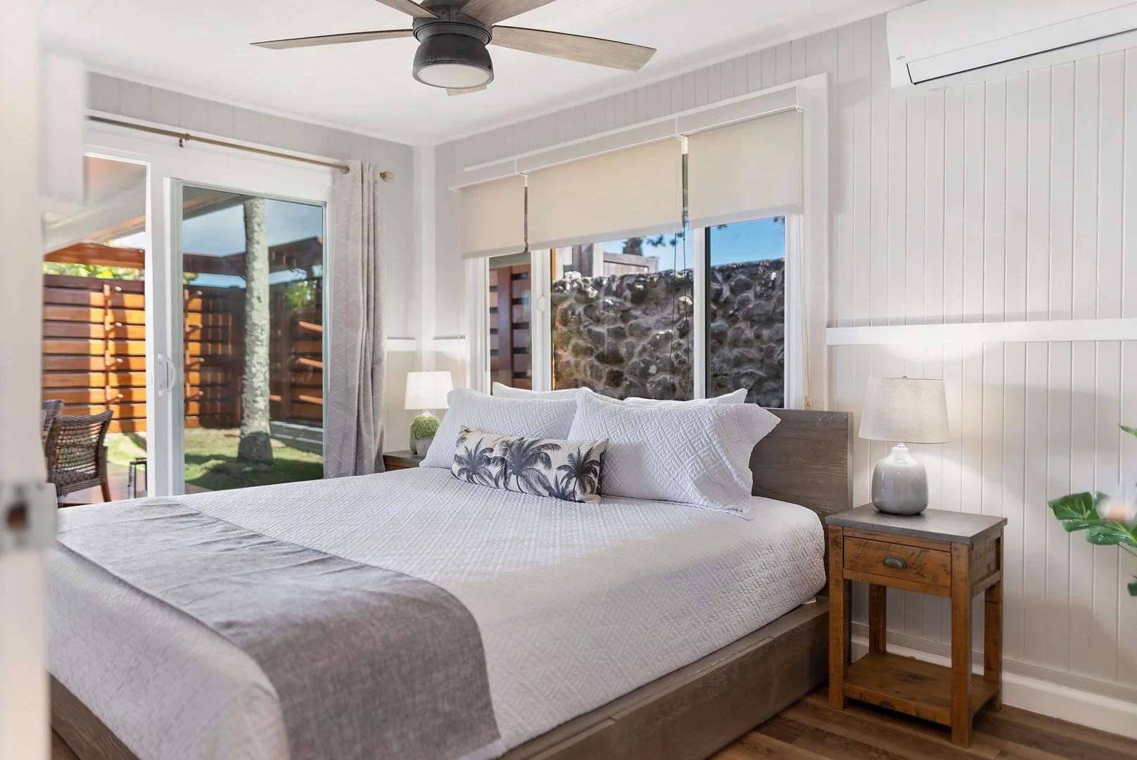 Un dormitorio luminoso con una cama tendida y ventanas con vistas a un muro de piedra.