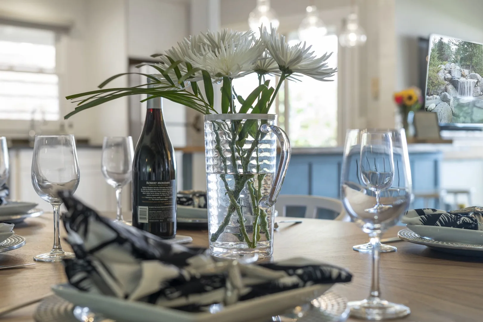 Una mesa de comedor está preparada con cristalería y un jarrón de flores blancas.