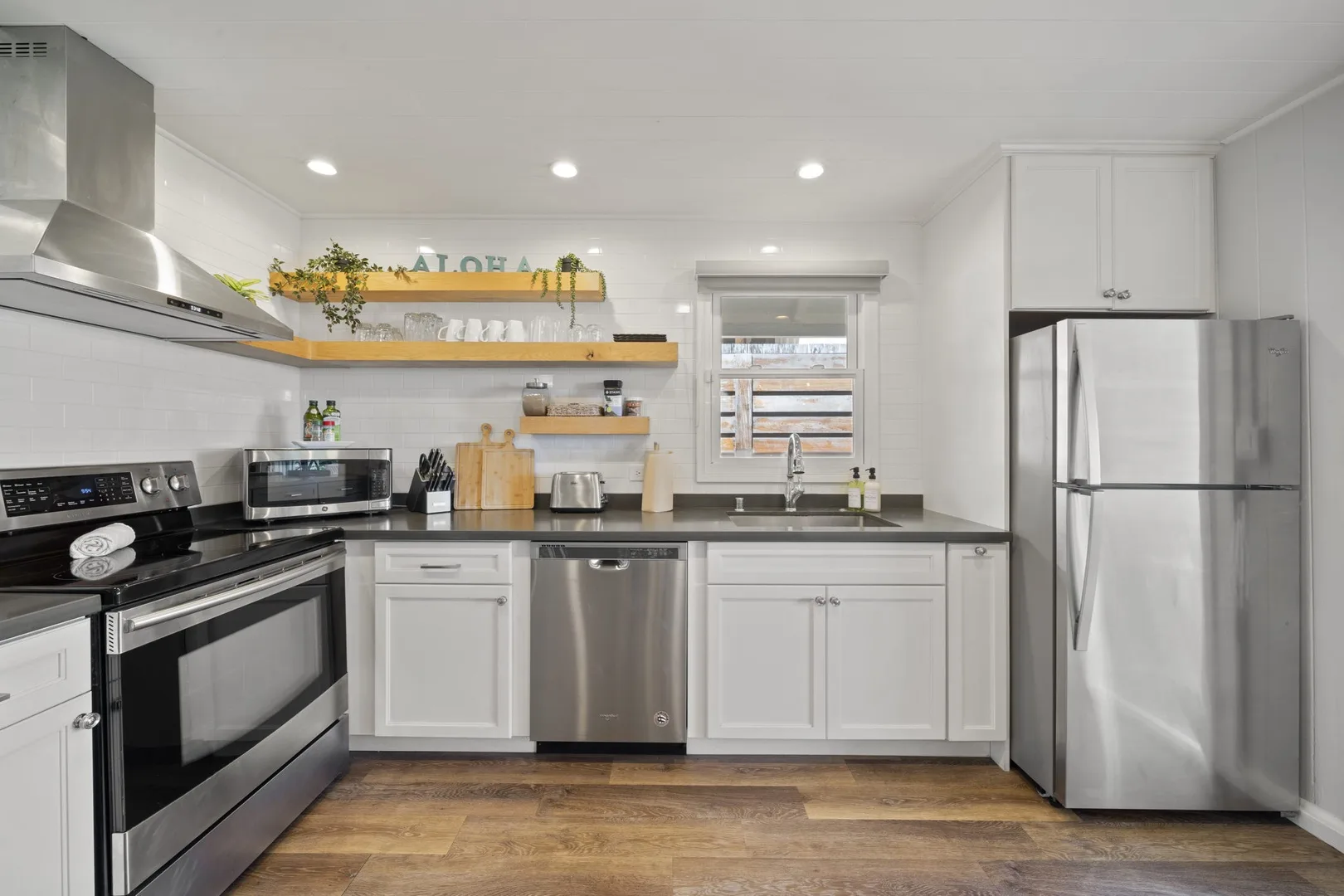 Una cocina luminosa con gabinetes blancos, electrodomésticos de acero inoxidable y una ventana central.