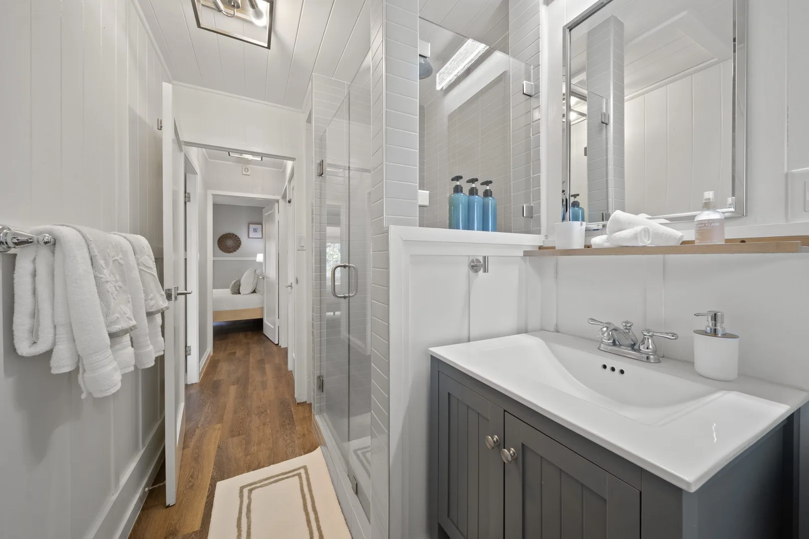 Un baño luminoso con lavabo, ducha de vidrio y pasillo.