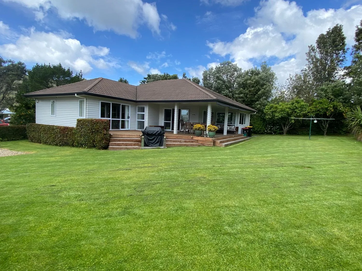 A house with a brown roof and white walls surrounded by a green lawn and trees at Hahei Haven - Hahei Holiday Home in Hahei