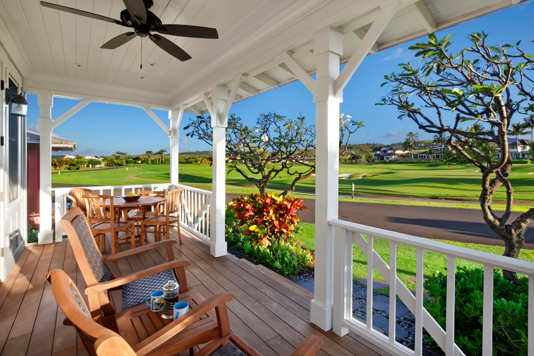 A covered outdoor porch with wooden seating overlooks a green golf course.