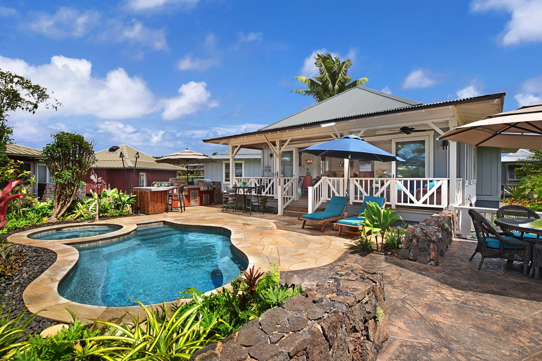 A tropical outdoor pool beside a covered patio with seating.