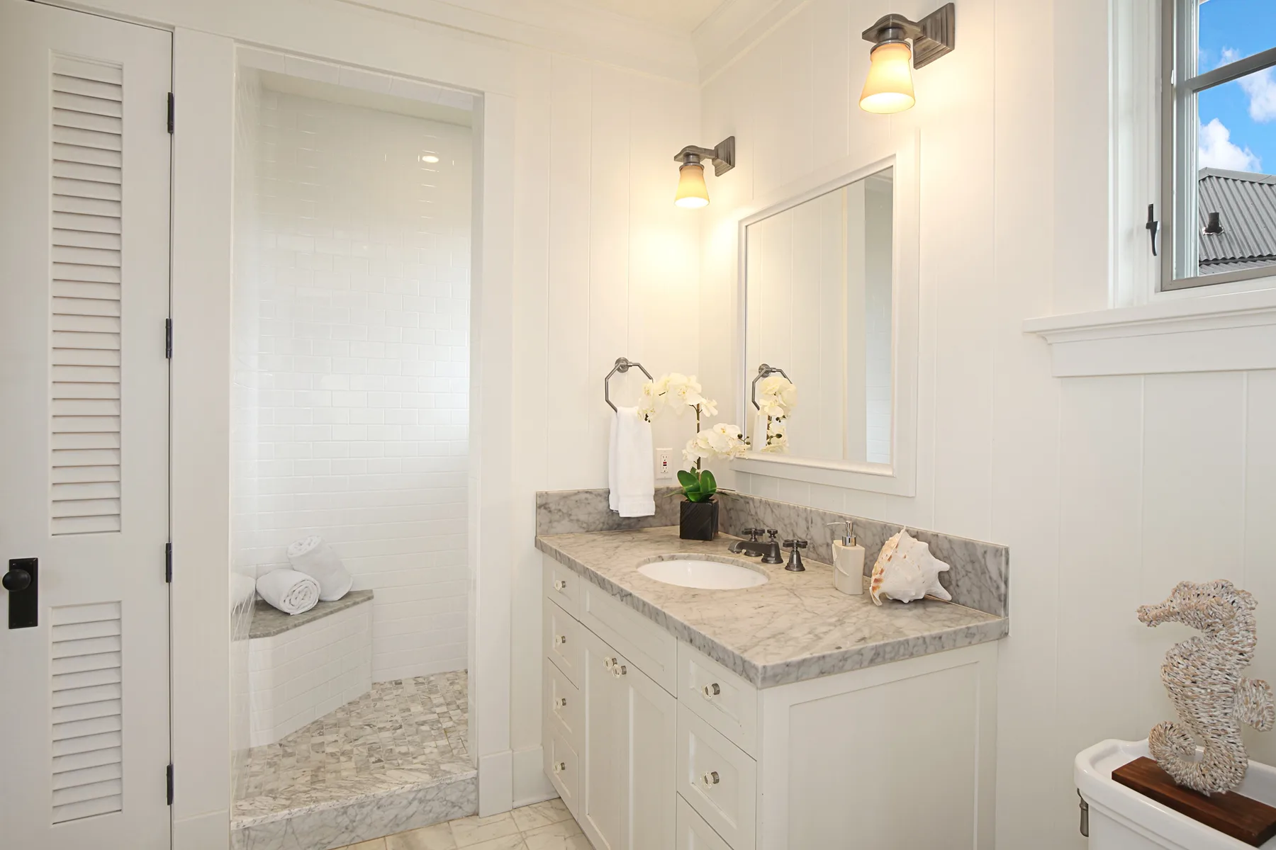 A bright bathroom with a long vanity, mirror, and walk-in shower.