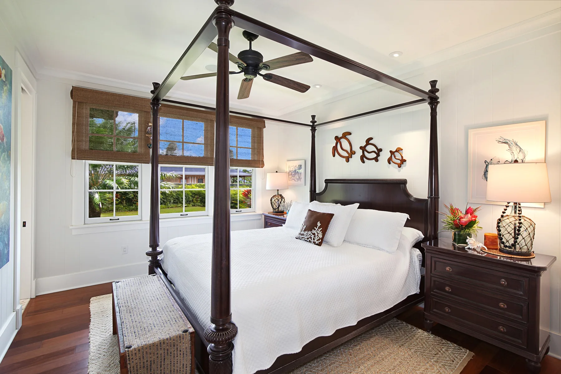A bright bedroom with a four-poster bed and windows overlooking greenery.
