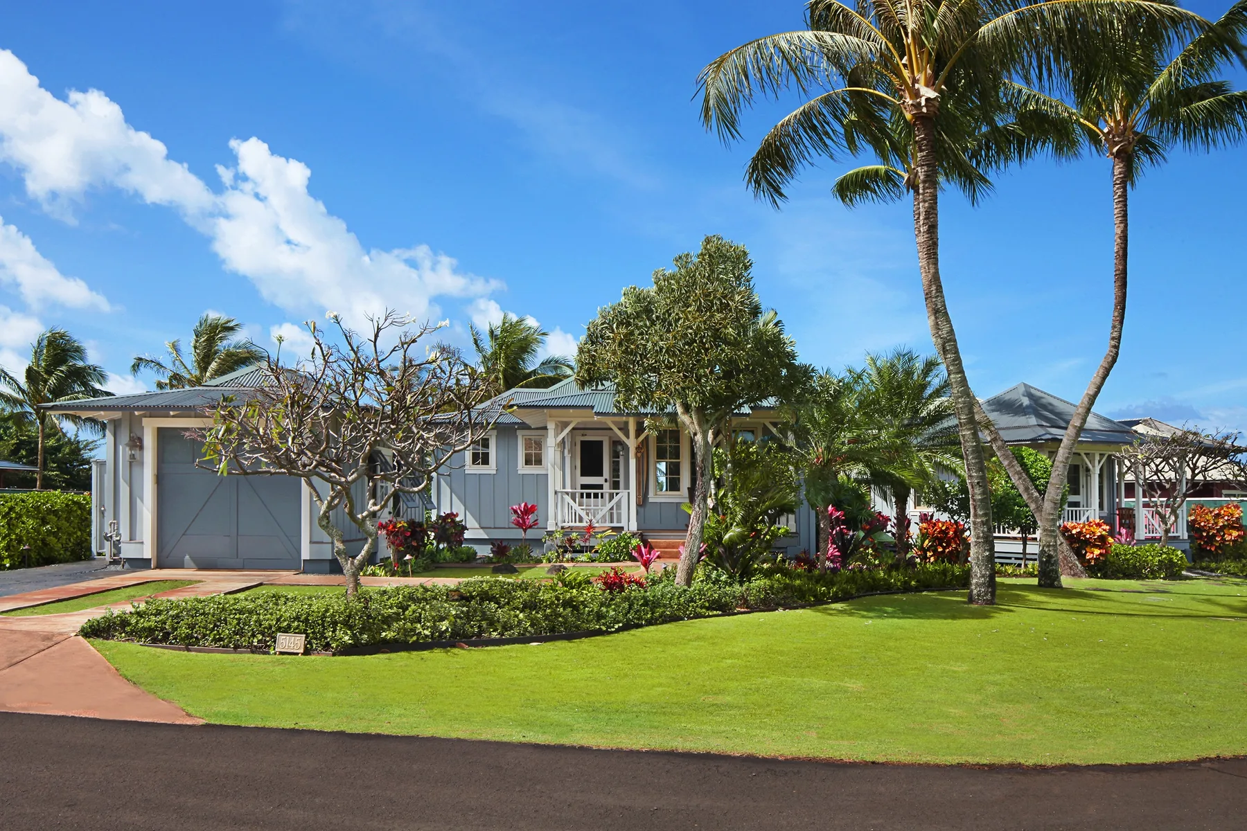 A single-story house sits behind a landscaped lawn with palm trees.