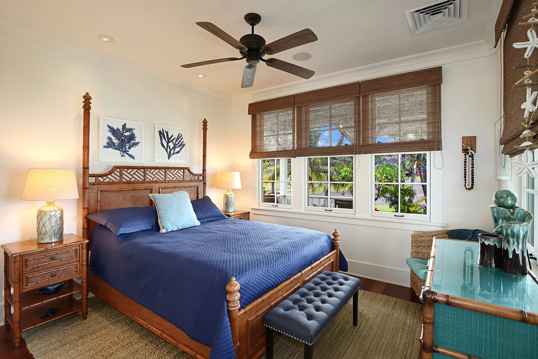 A bedroom with a blue bed beneath windows with woven blinds.