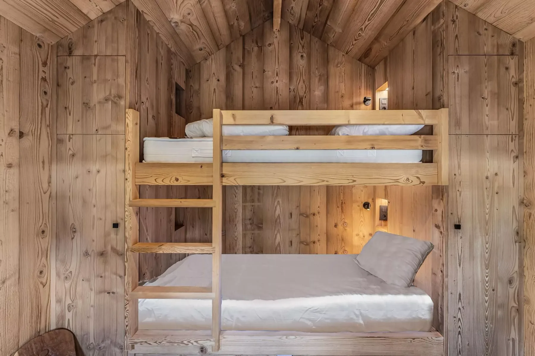Una litera de madera ocupa un dormitorio pequeño con paredes revestidas de madera.