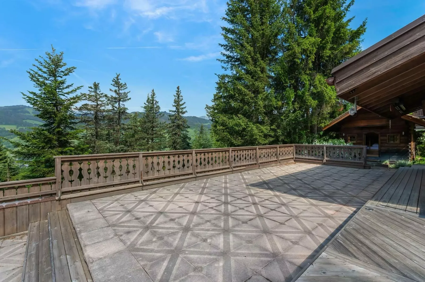 Una amplia terraza exterior con pavimento estampado, barandillas de madera y árboles alrededor.