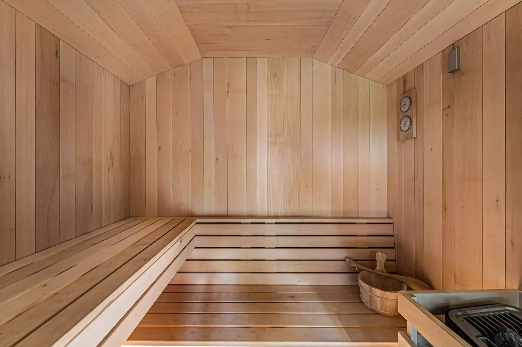 Una sauna revestida de madera, con asientos escalonados y un termómetro en la pared.