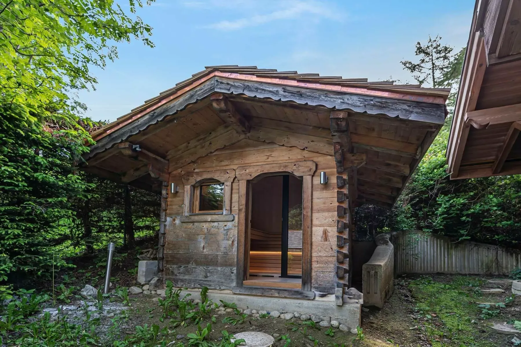 Una pequeña cabaña de madera está entre árboles, con la entrada abierta a la vista.