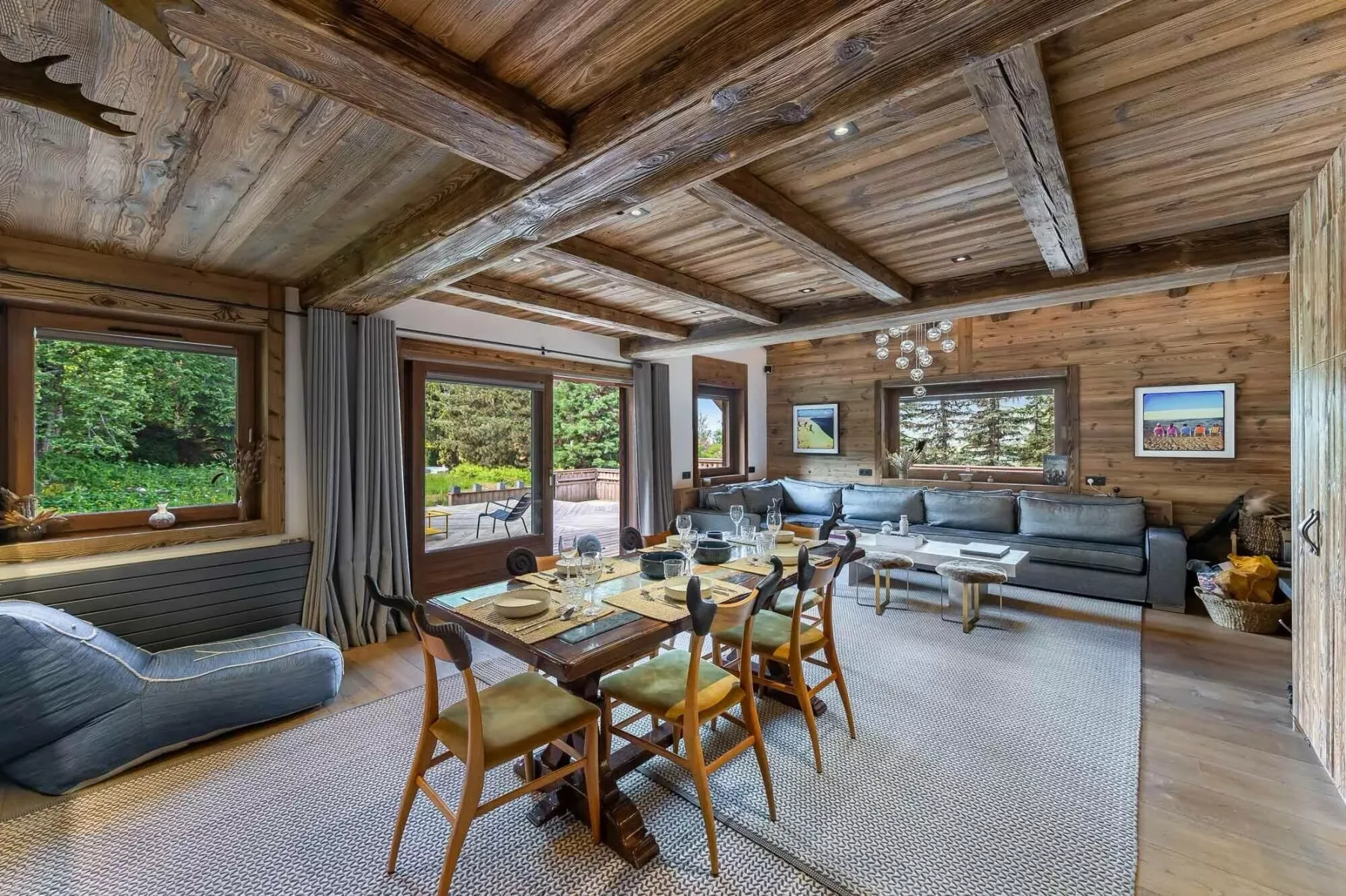 Una sala con paredes de madera tiene una mesa de comedor, asientos y ventanales.