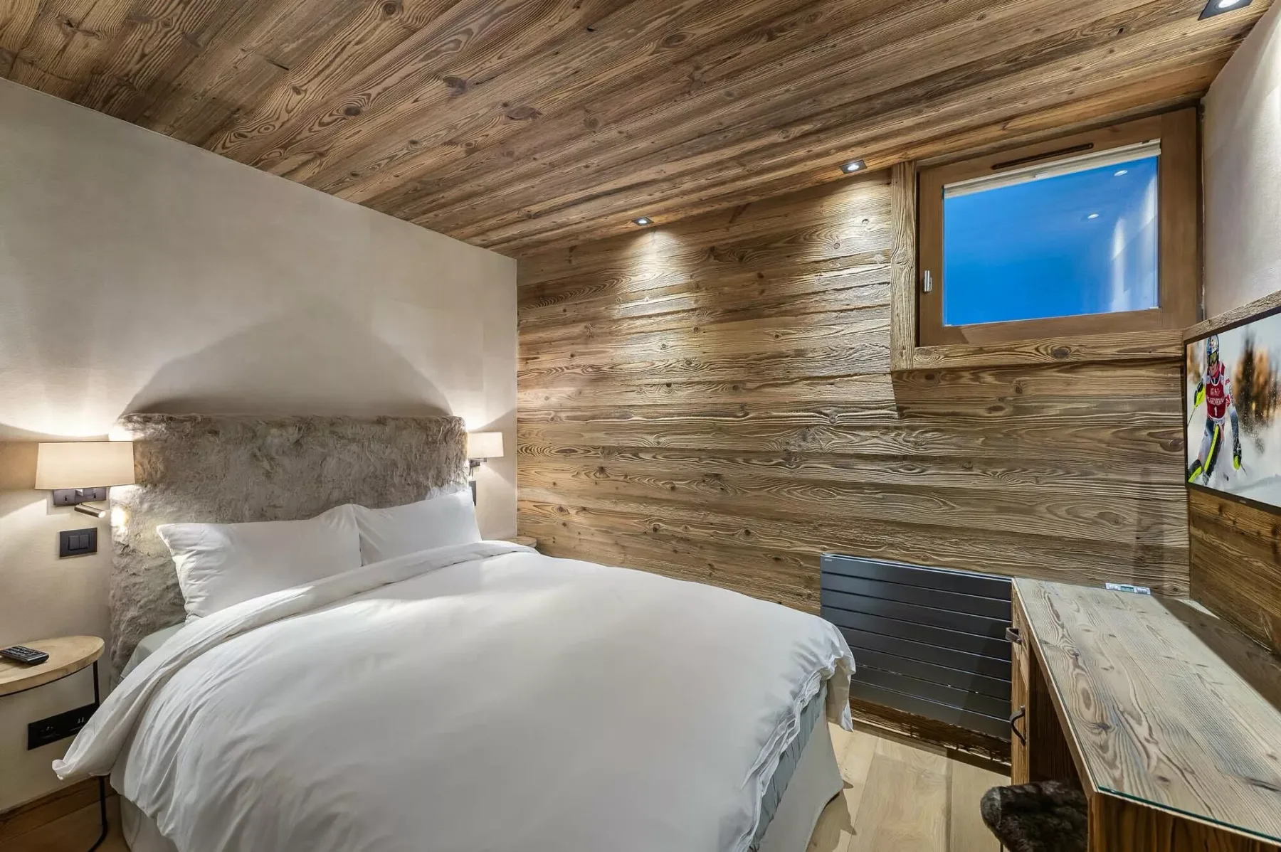 Un dormitorio con una cama, paredes revestidas de madera y una ventana pequeña.