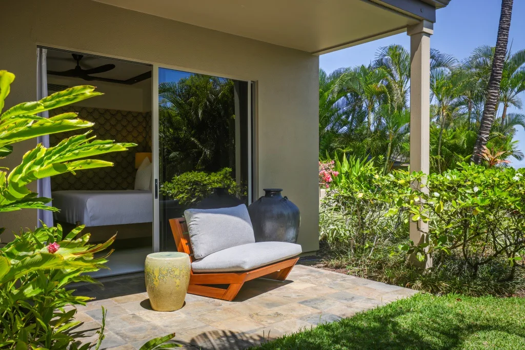 Un patio cubierto con asientos acolchados da a una frondosa vegetación tropical.