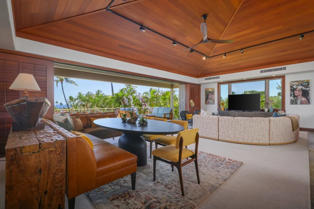 Una amplia sala de estar con asientos alrededor de una mesa y grandes ventanas con vista a la vegetación.