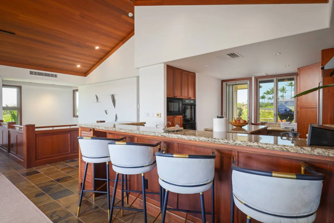Una cocina abierta con una isla larga y asientos de barra bajo un techo revestido de madera.