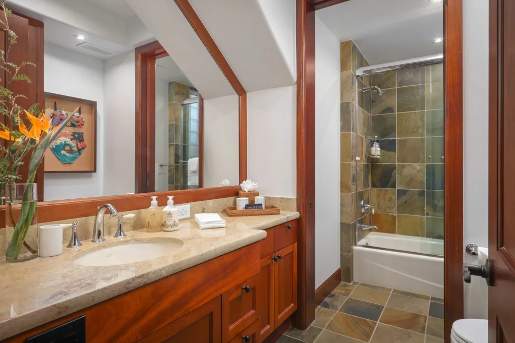 Un tocador de baño con espejo está junto a una ducha revestida de azulejos y una bañera.