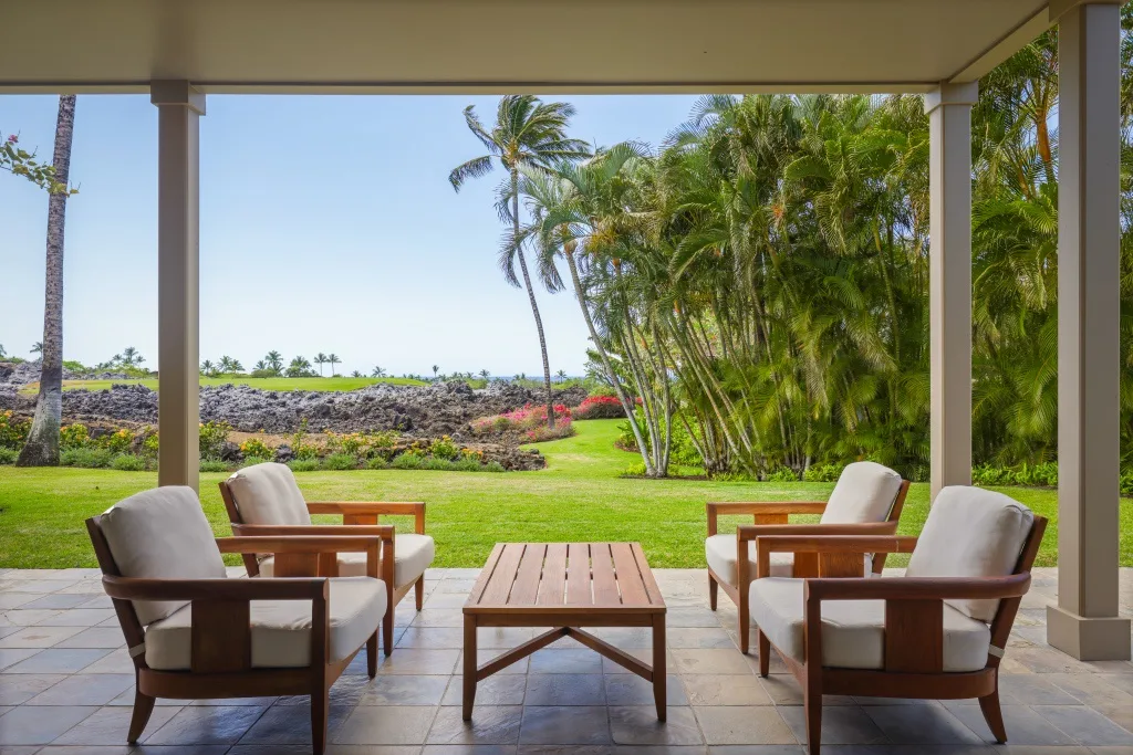 Un patio cubierto con asientos acolchados y vistas a un jardín verde.