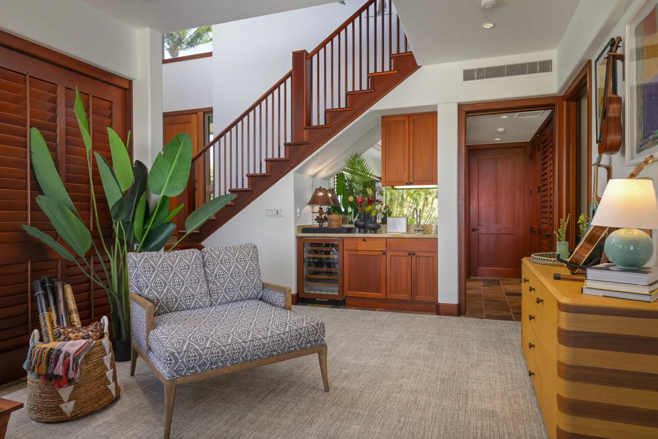 Una sala de estar con un asiento estampado, una escalera y una pequeña cocina.