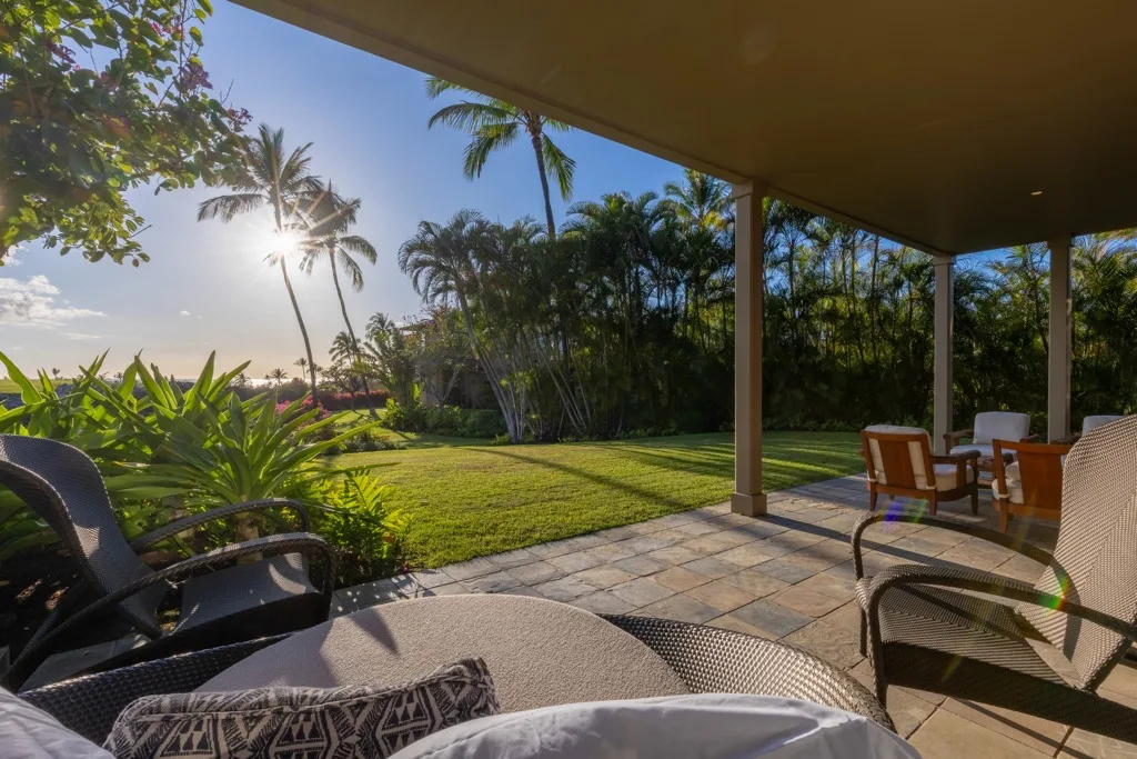 Un patio cubierto da a un césped verde y a vegetación tropical.