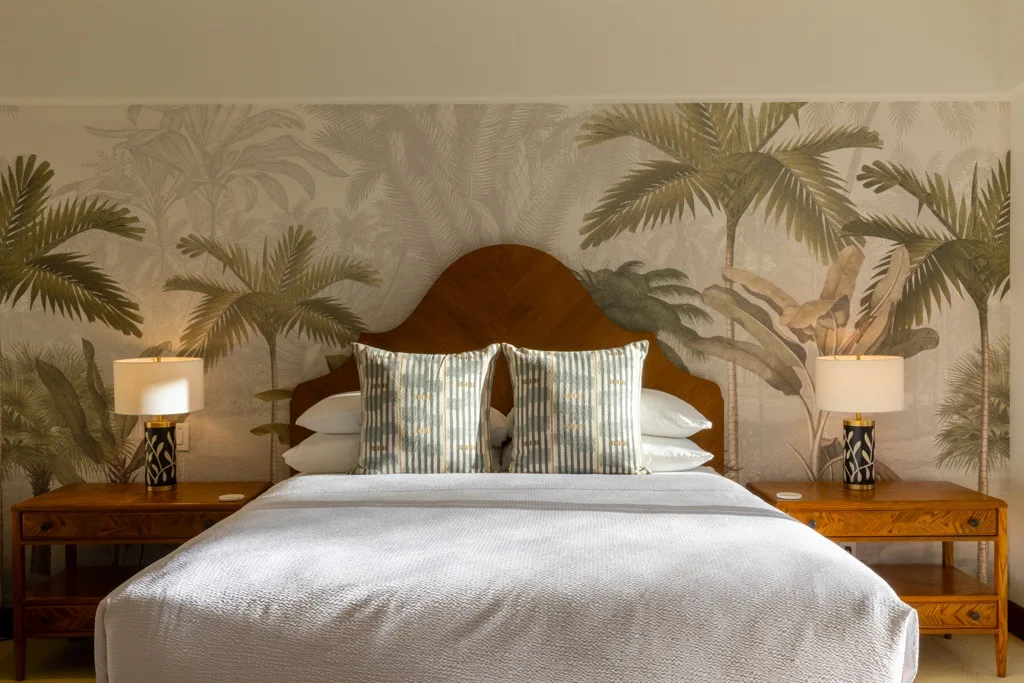 Un dormitorio con una cama bien arreglada frente a un mural de palmeras tropicales.