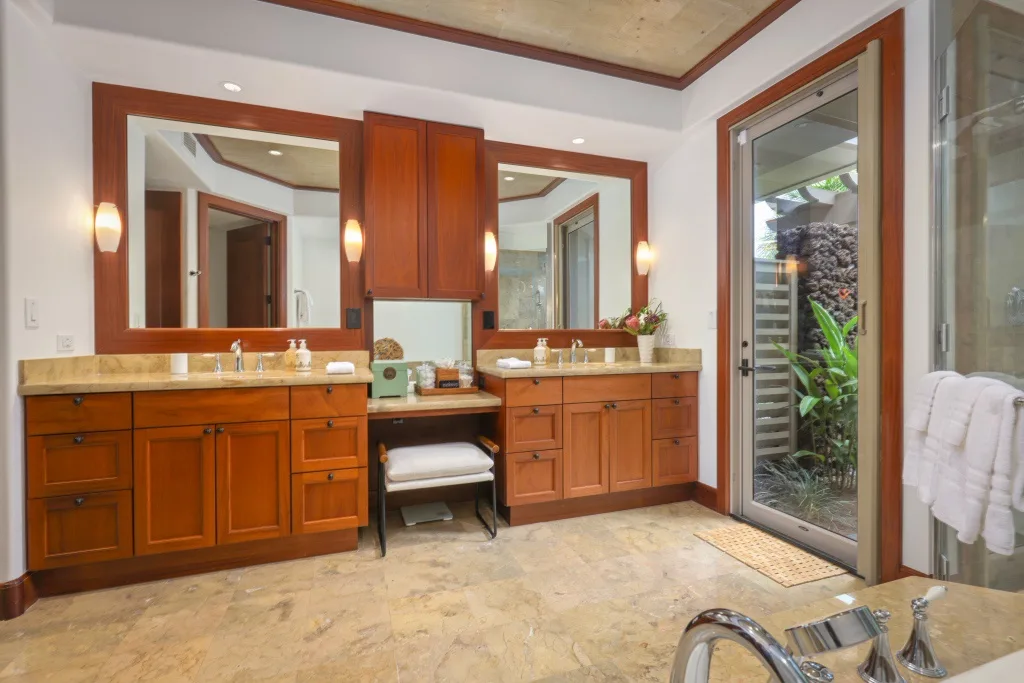 Un tocador de baño con gabinetes de madera, espejos y una puerta de vidrio junto a la vegetación.
