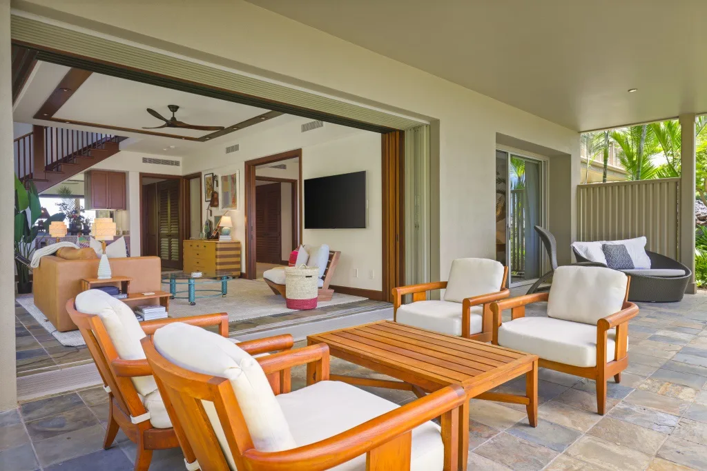 Una sala amueblada se abre a un patio cubierto con asientos acolchados y una mesa de madera.