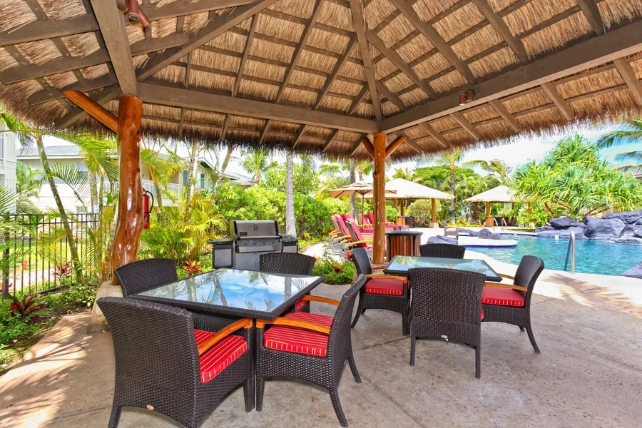 A covered outdoor dining area with seating beside a swimming pool.
