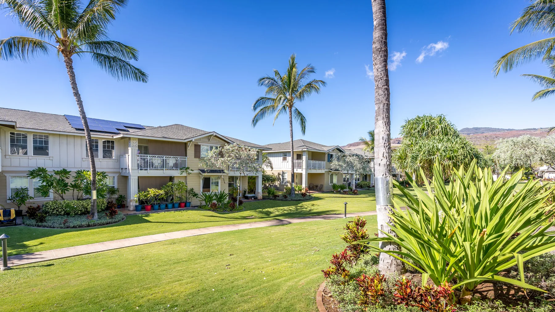 A landscaped residential complex with low-rise buildings, palm trees, and green lawns.