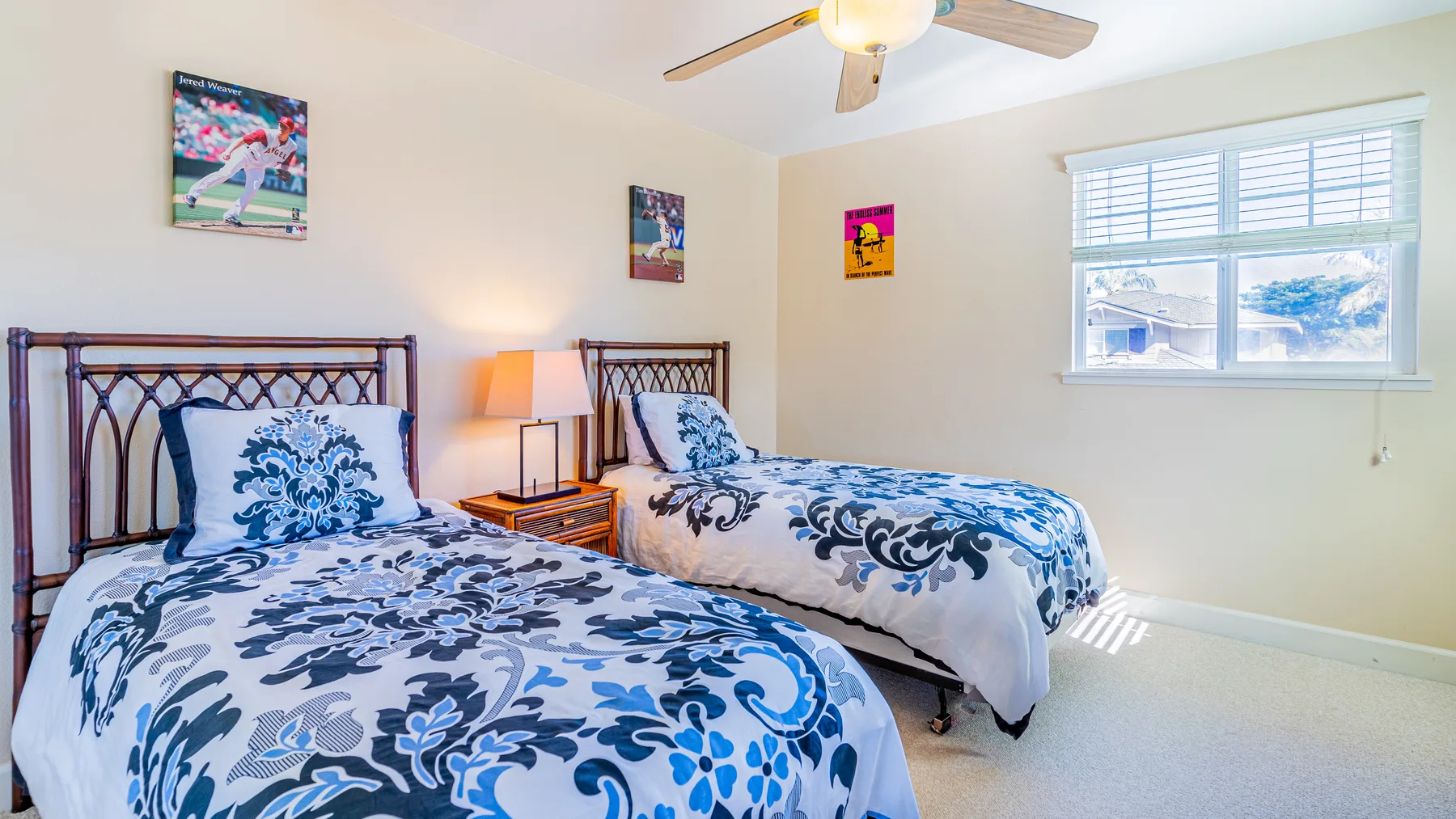 A bedroom with two beds, patterned bedding, and a window with blinds.
