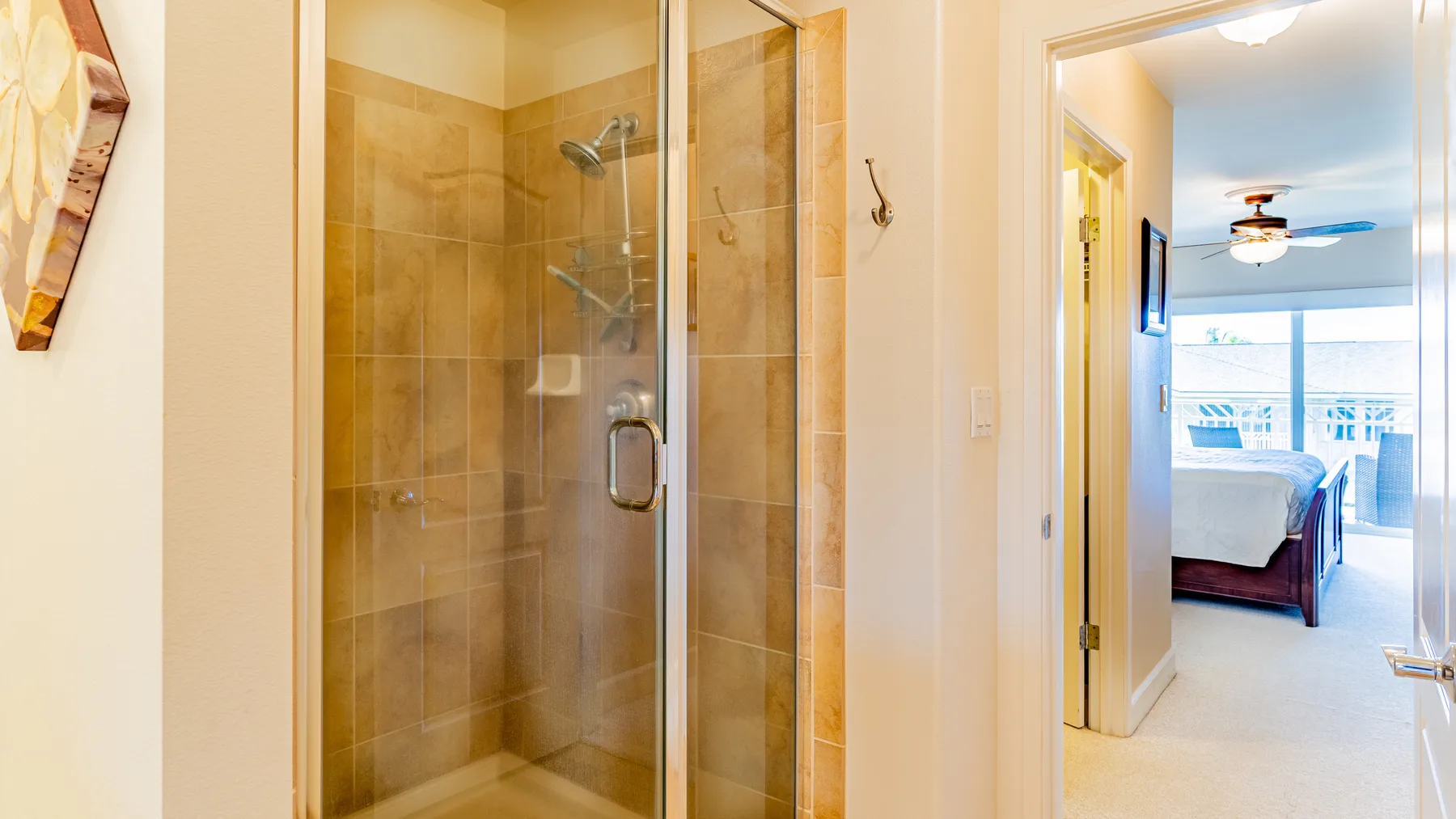 A tiled shower stands beside an open doorway to a bedroom.