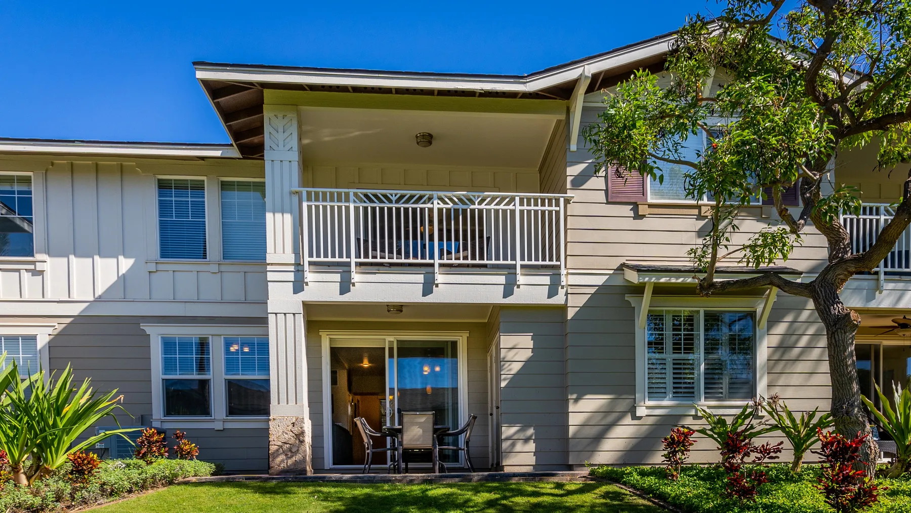 A two-story house exterior with a covered upper balcony and ground-level patio.