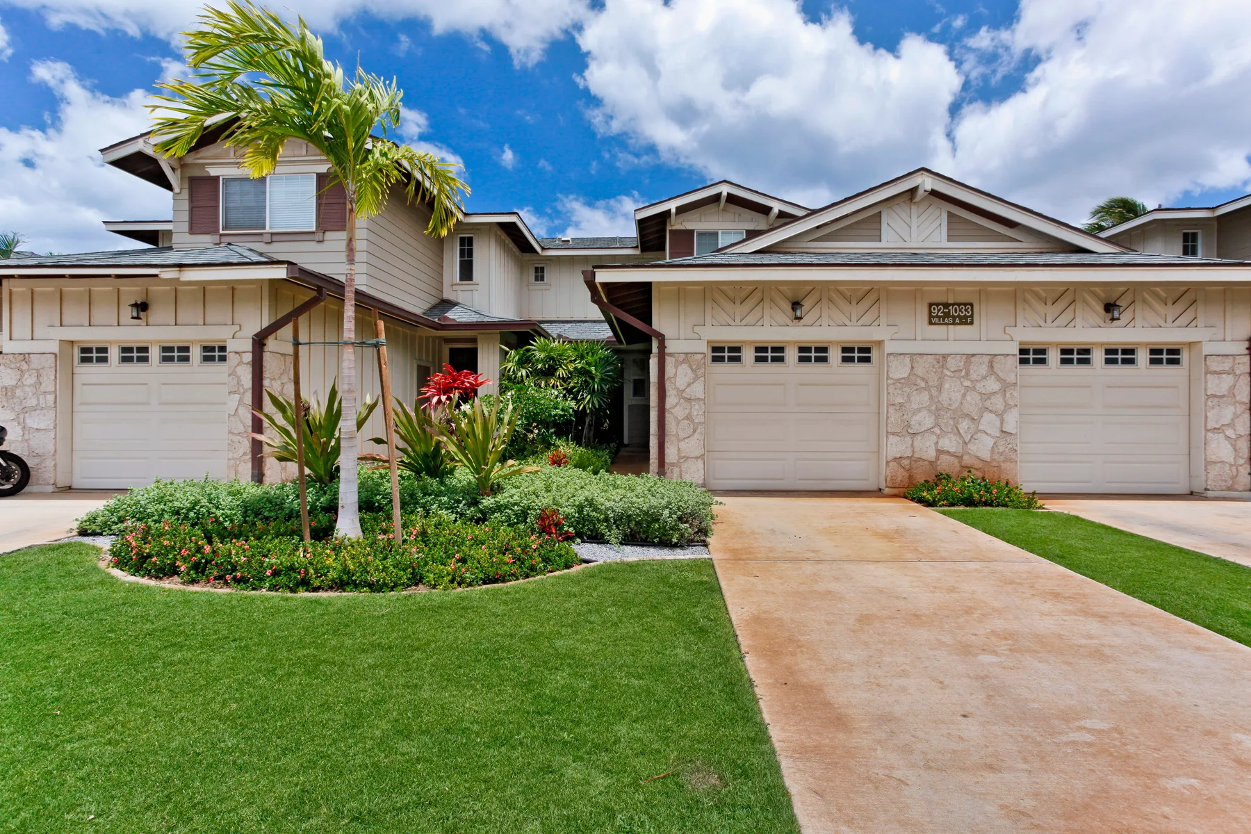 A row of attached homes with garages, landscaped gardens, and a paved driveway.