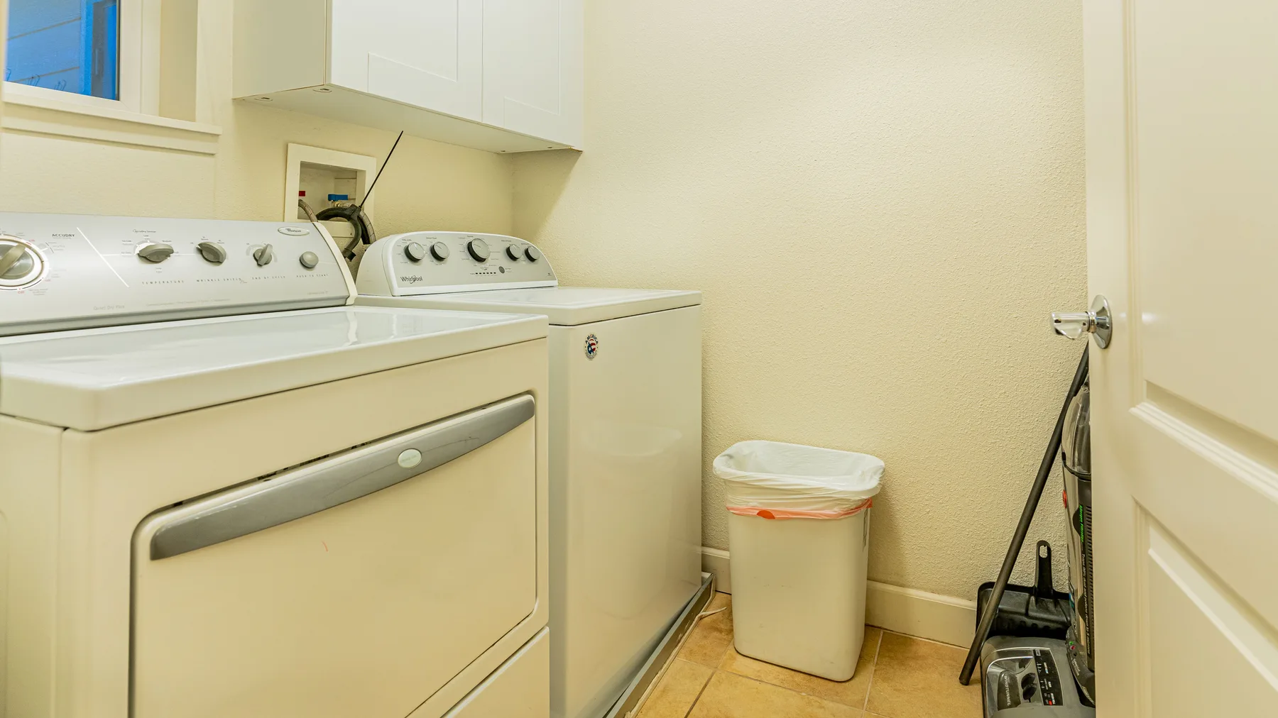 A laundry room with a washer, dryer, and small waste bin.