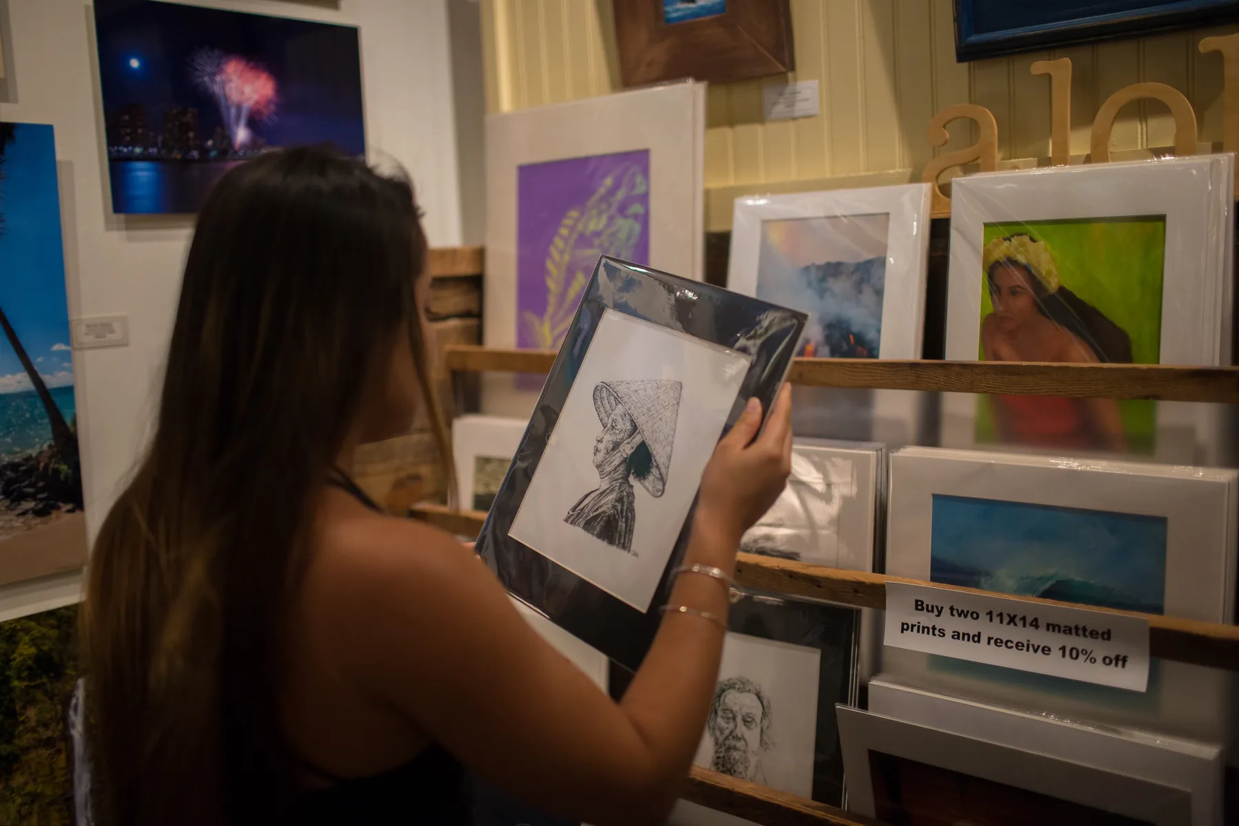 A woman browses framed prints displayed on wooden shelves in an art gallery.