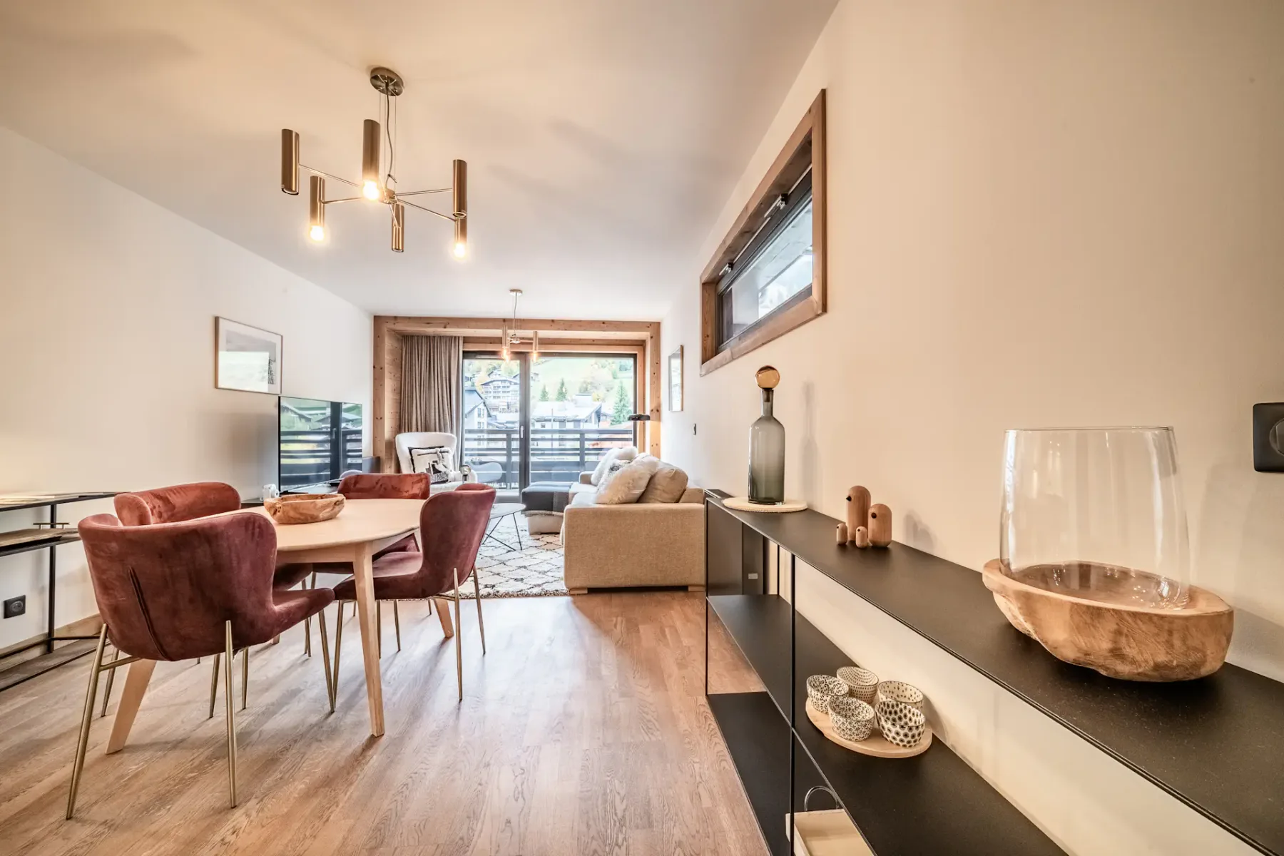 Modern, minimalist kitchen with white cabinets, built-in oven, and a small sink. There is a table with red chairs and a lamp in the background, with soft lighting creating a cozy atmosphere.