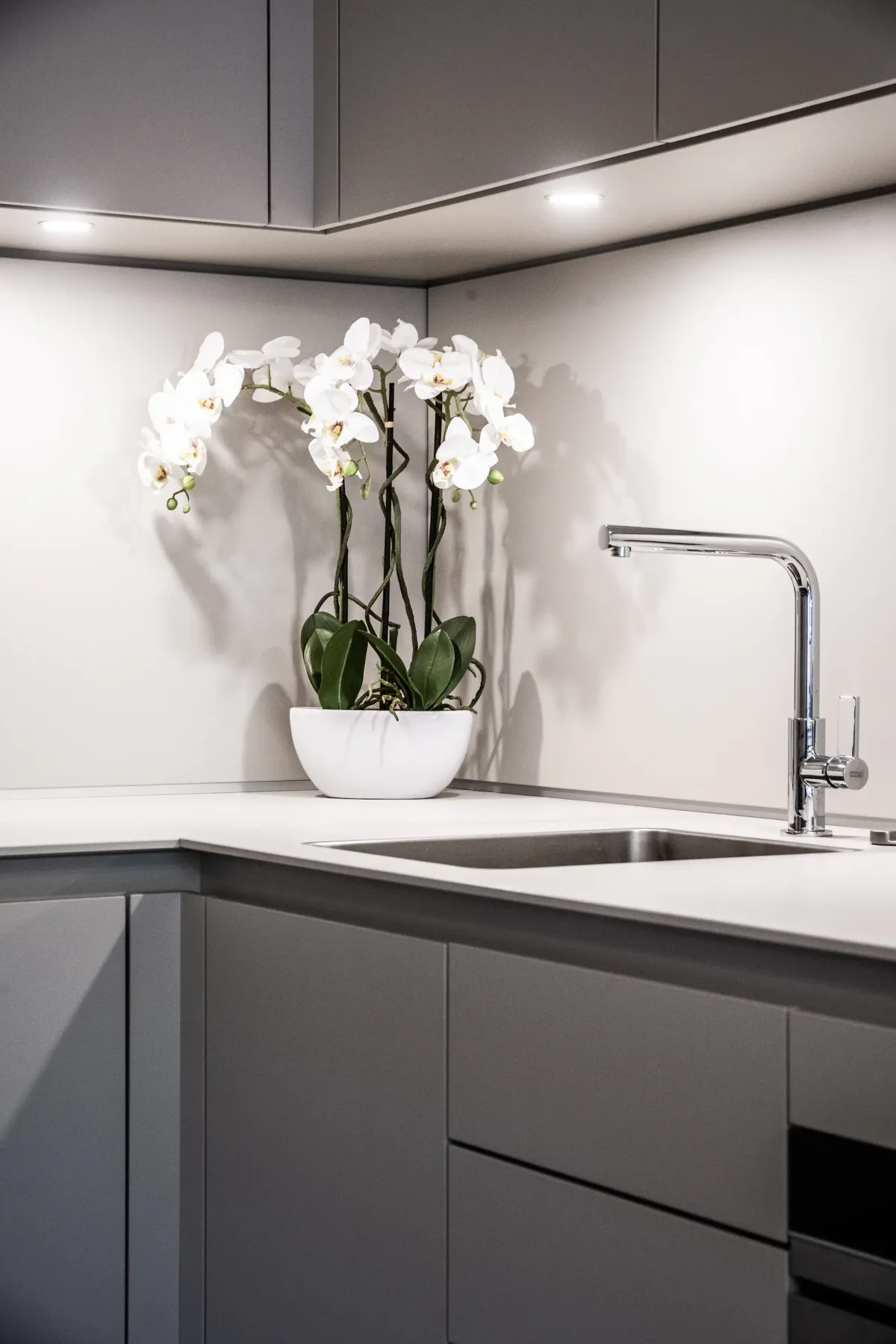 Modern, minimalist kitchen with white cabinets, built-in oven, and a small sink. There is a table with red chairs and a lamp in the background, with soft lighting creating a cozy atmosphere.