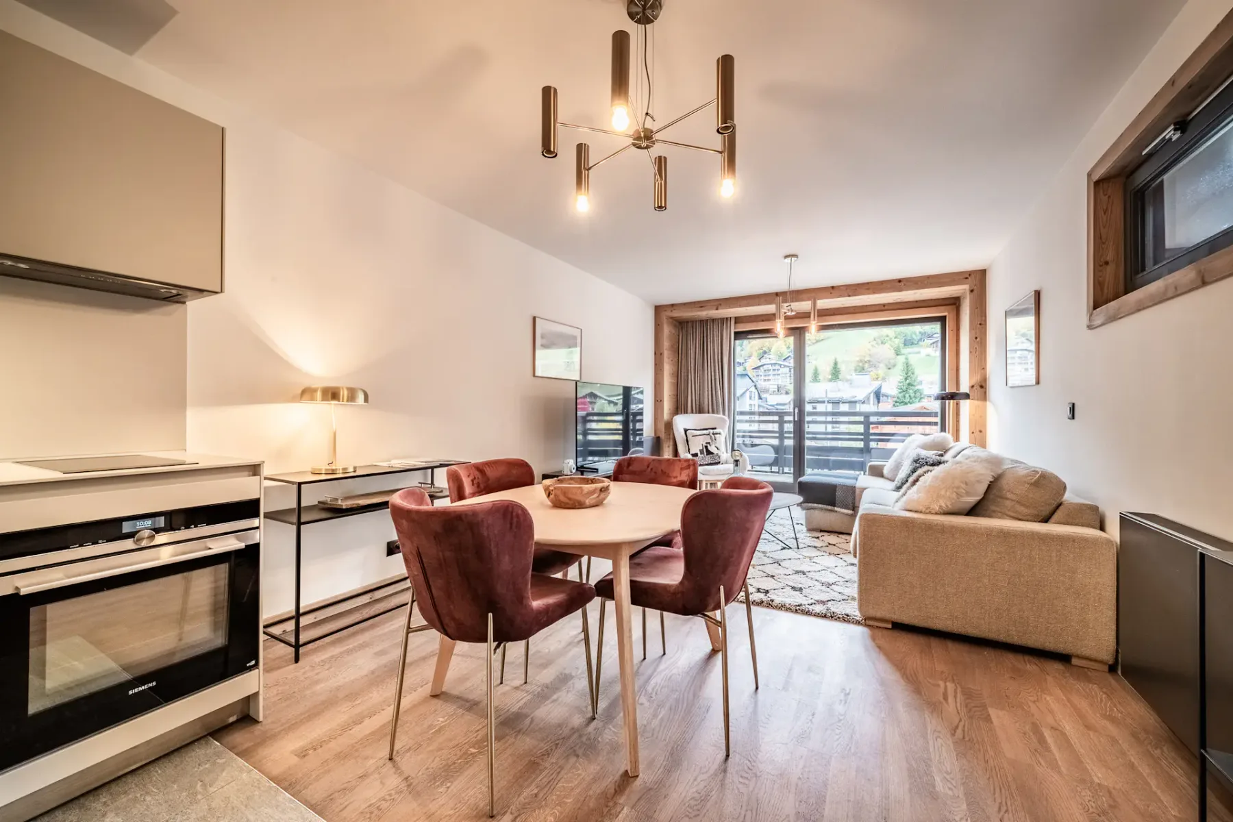 Modern, minimalist kitchen with white cabinets, built-in oven, and a small sink. There is a table with red chairs and a lamp in the background, with soft lighting creating a cozy atmosphere.