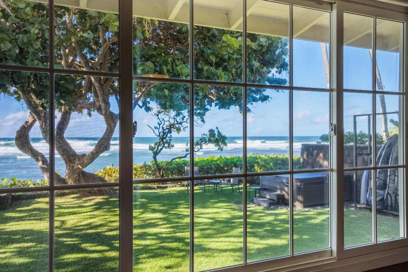 Large windows overlook a green lawn, leafy trees, and the ocean.