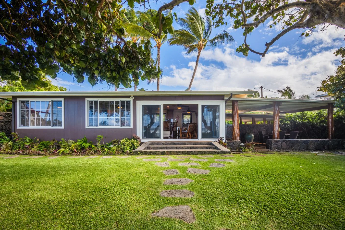 A low modern house opens onto a green lawn with a stone path.
