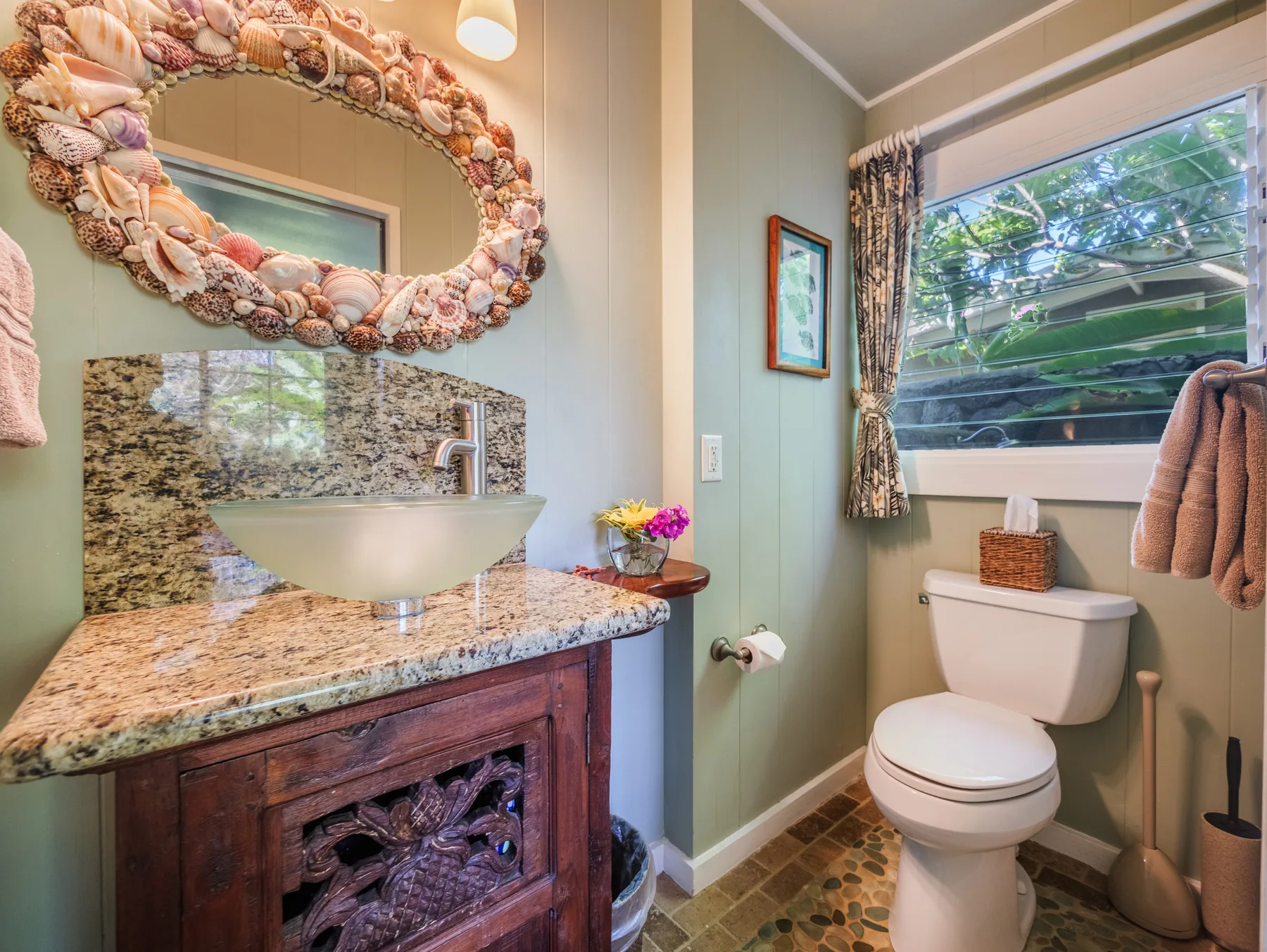 A bathroom with a sink vanity and a toilet beside a window.