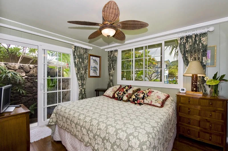 A bedroom with a large bed, patterned bedding, and windows overlooking greenery.