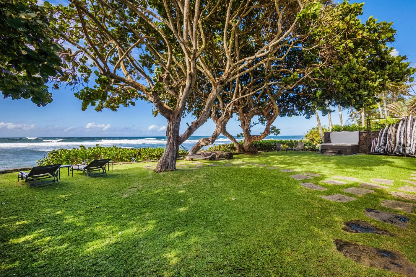 A grassy seaside lawn with shade trees and outdoor seating overlooks the ocean.