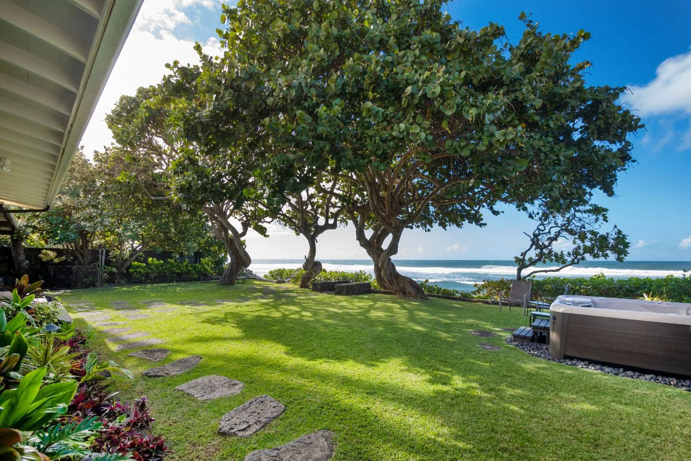 A grassy seaside yard has mature trees and a view of the ocean.