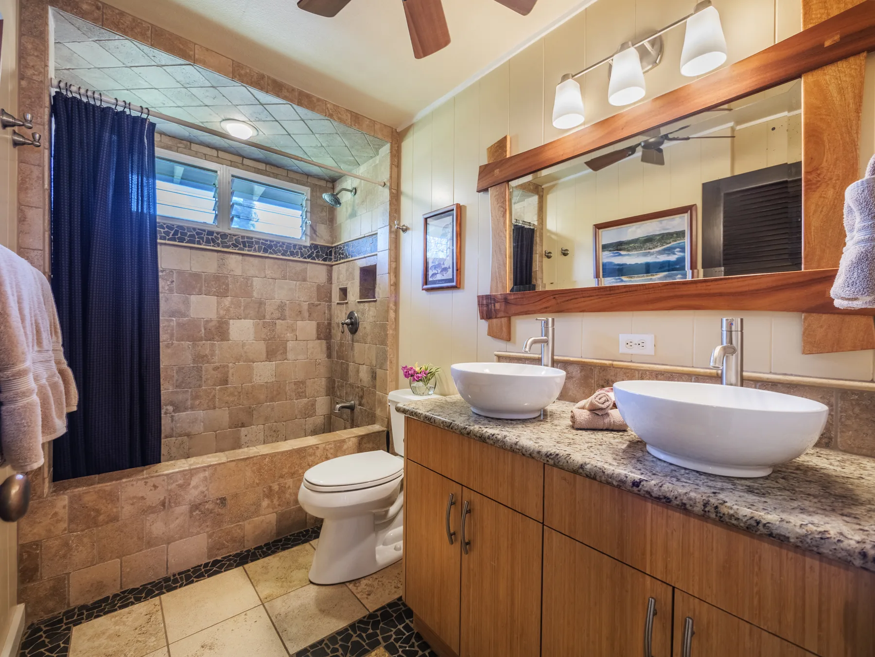 A bathroom with a tiled shower, toilet, and double-sink vanity.