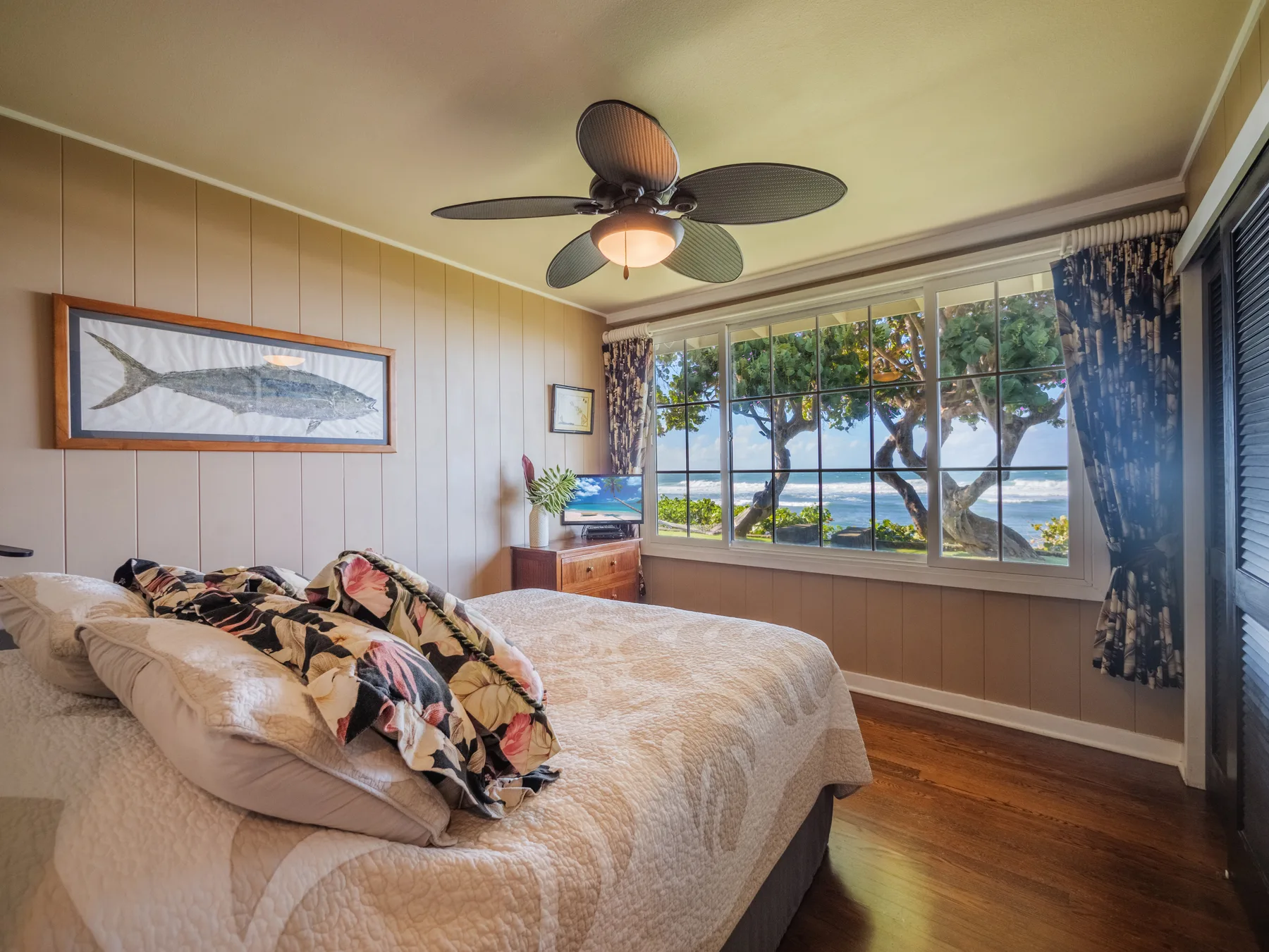 A bedroom with a bed beside large windows overlooking trees and water.