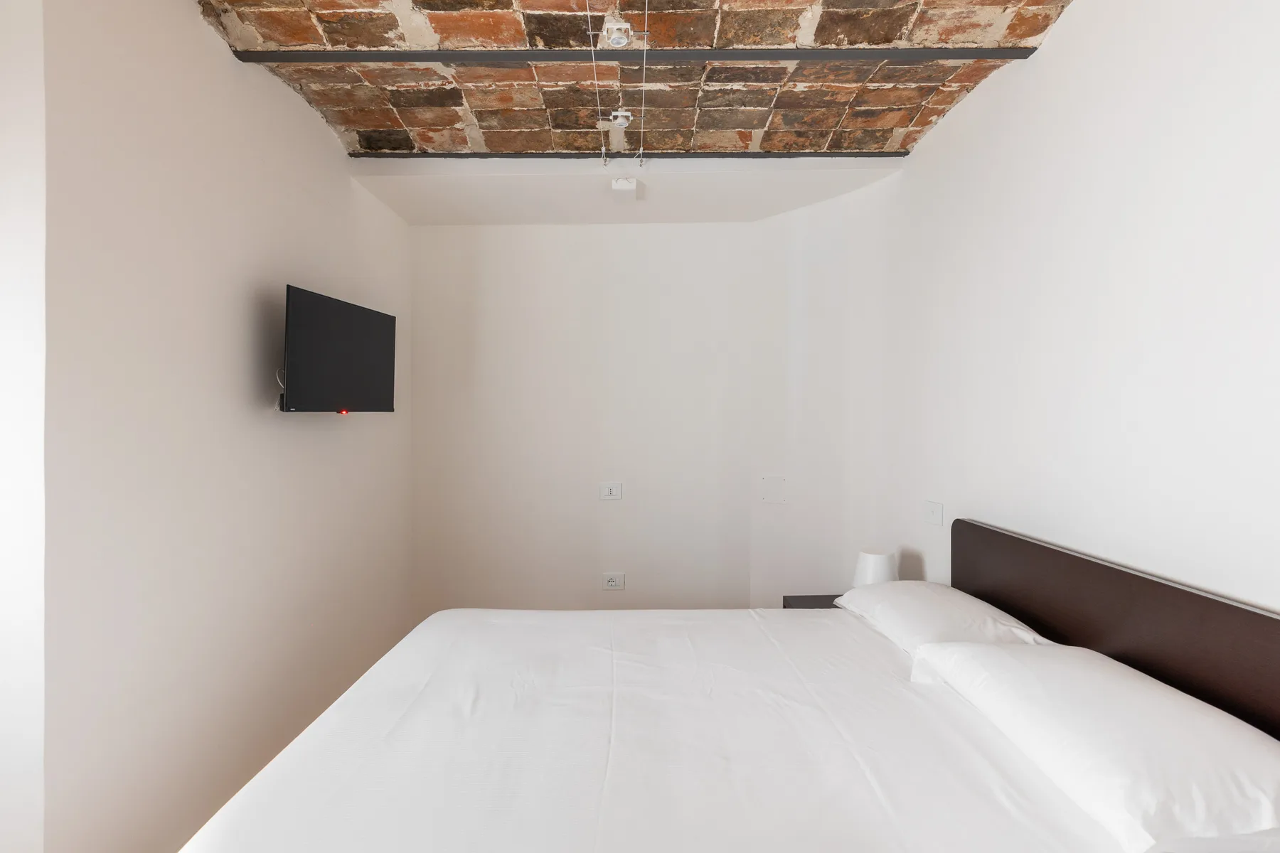 A bedroom with a bed beneath a rustic exposed-brick ceiling.